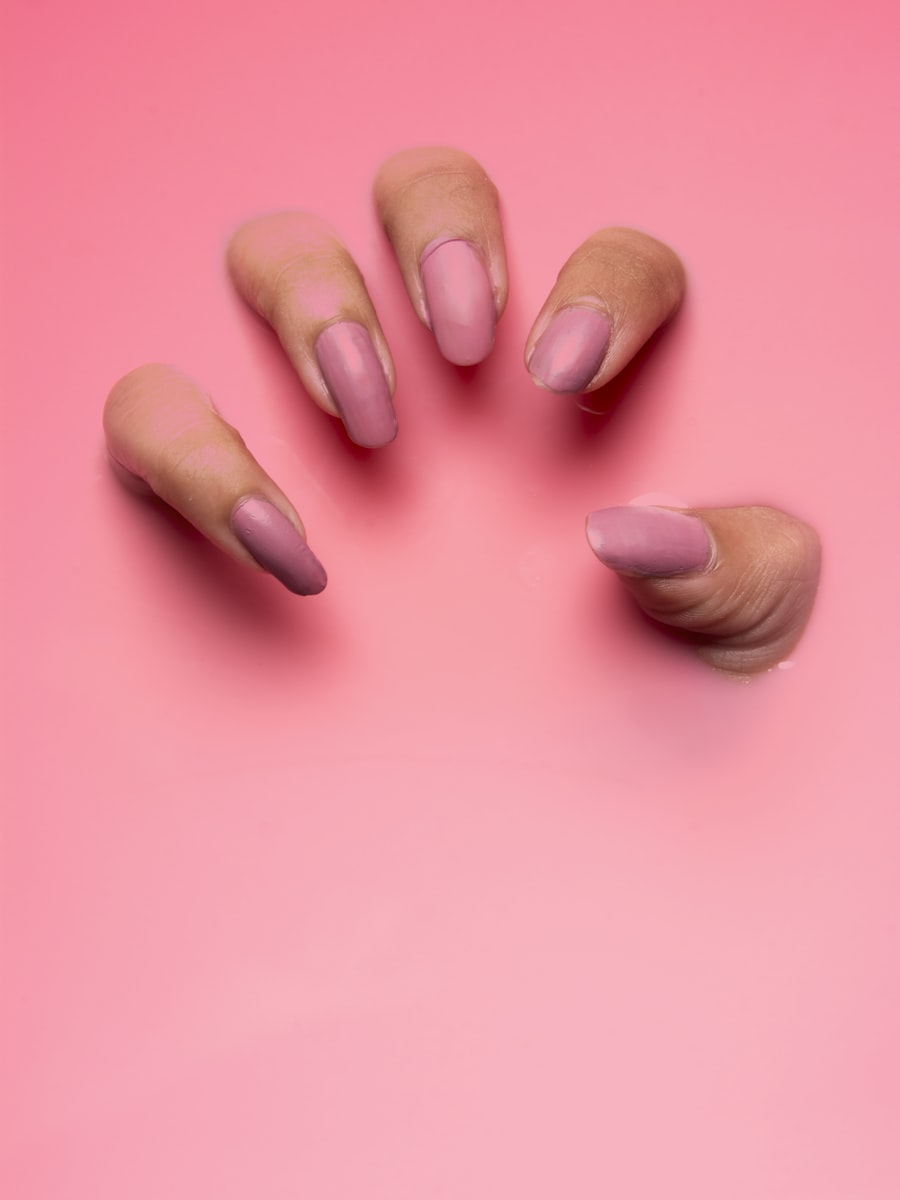 Hands with long soft pink almond-shaped nails against a bright pink background