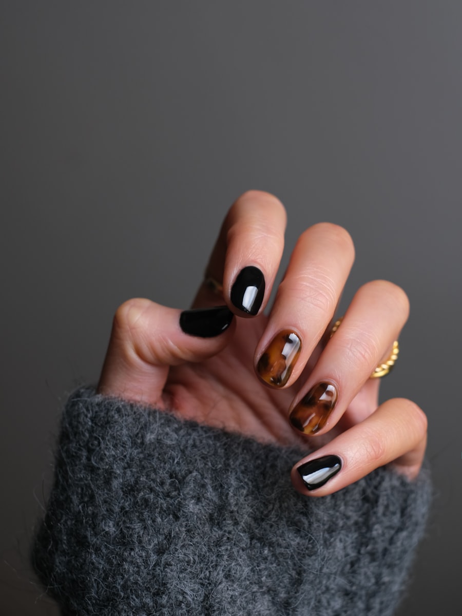 Hand with glossy black nails and two tortoiseshell patterned accent nails
