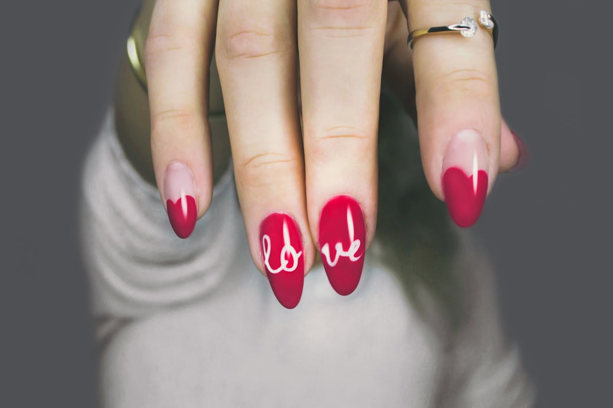 Hand with deep red nails featuring white hand-painted script lettering