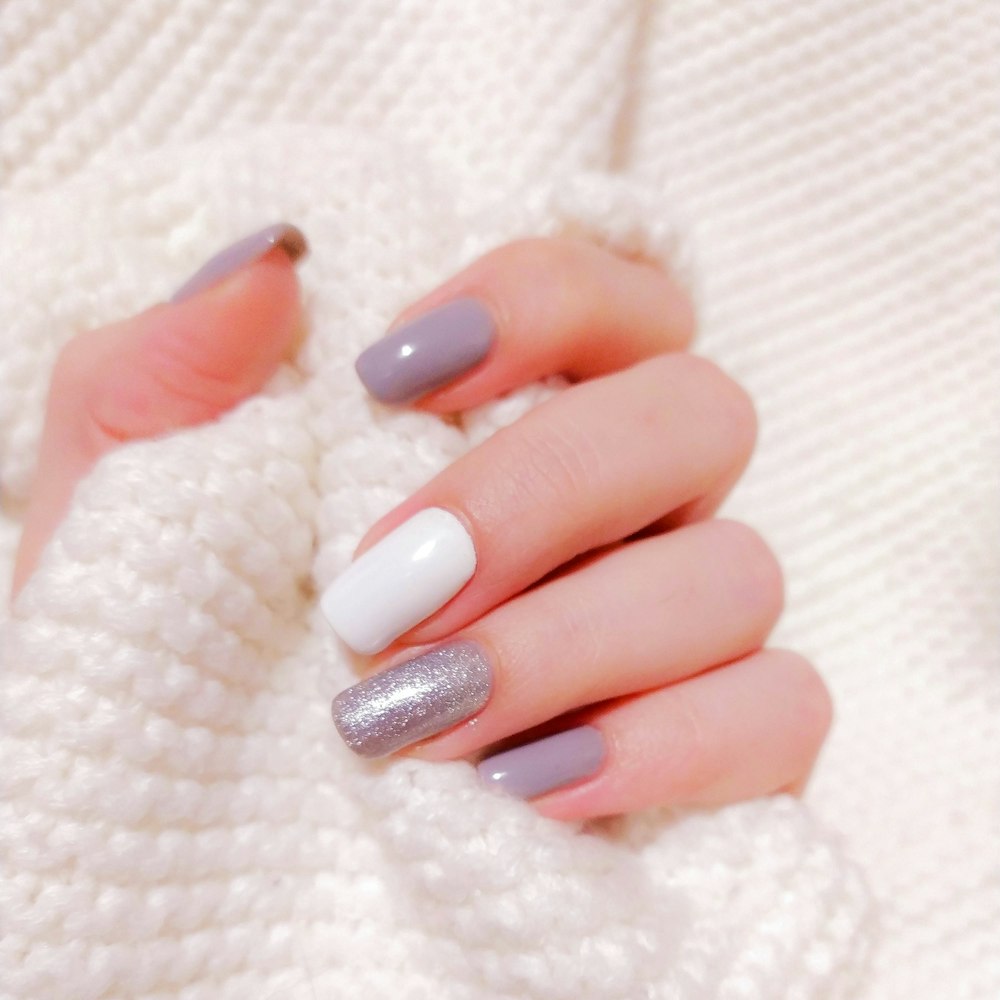 Hand resting on a cream knit sweater with grey, white and glitter square nails