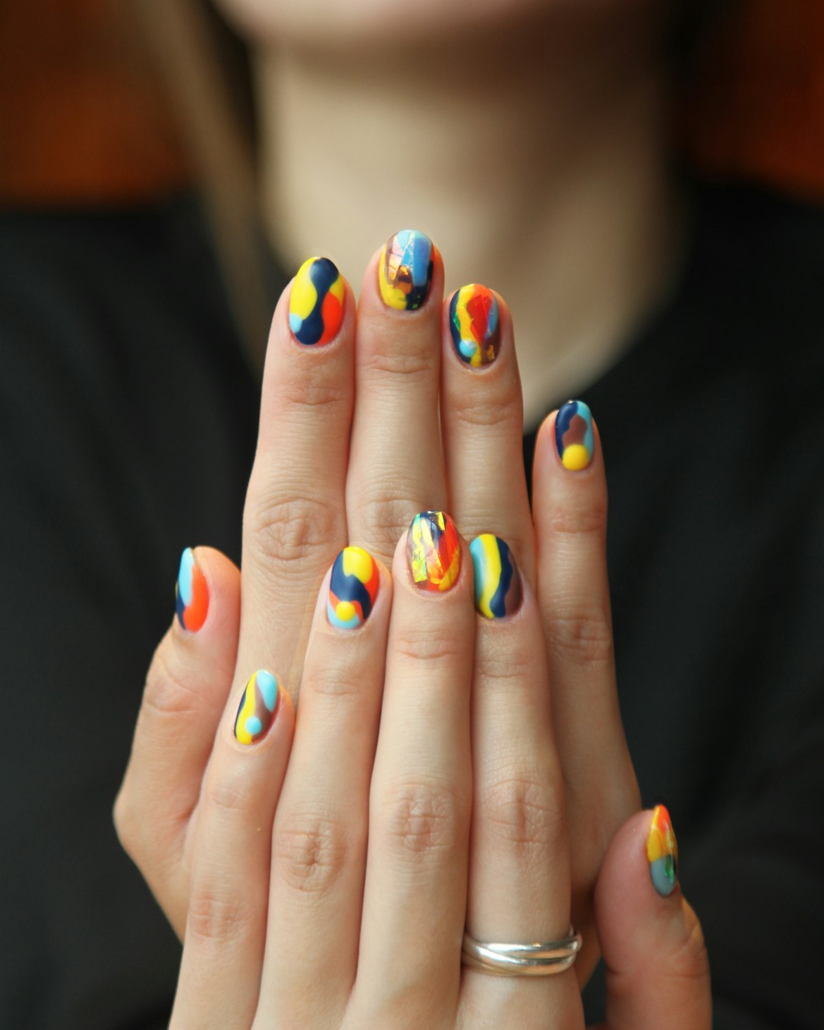 Hands raised showing a bright multicolour abstract freehand nail art set